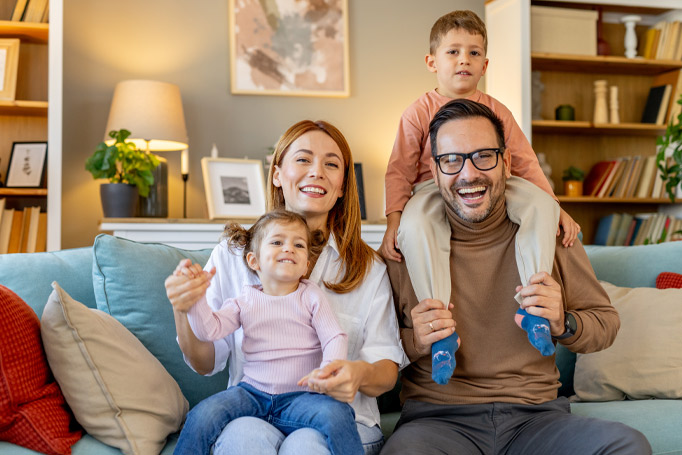 Mother holding daughter on her lap and father holding son on his shoulders while sitting on the couch