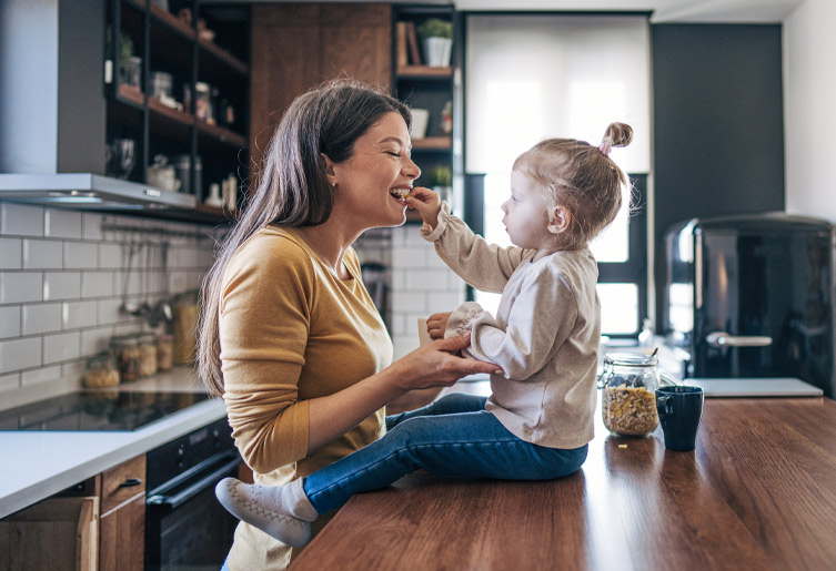 Daughter sitting on kitchen counter feeding her mother a snack