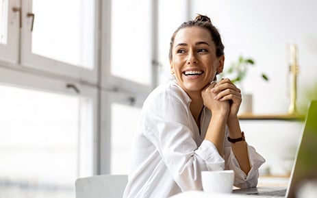 Woman in white blouse smiling looking away from laptop