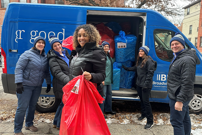 Volunteers standing in front of the giving for good van with one volunteer holding a red bag